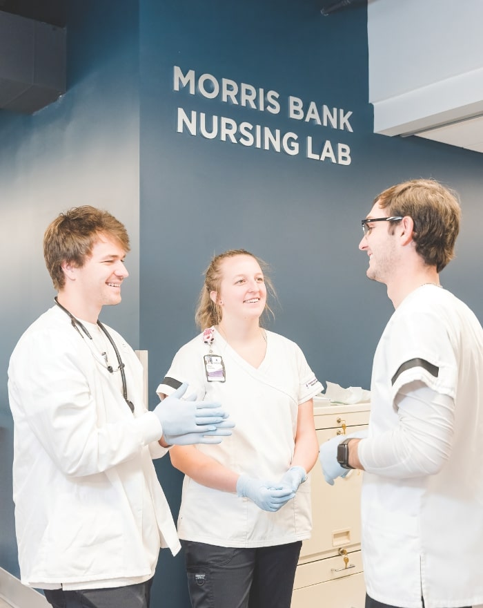 Three students under the Morris Bank Nursing Lab sign 